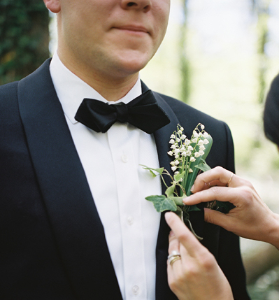 Bride pinning lily of the valley boutonniere on groom