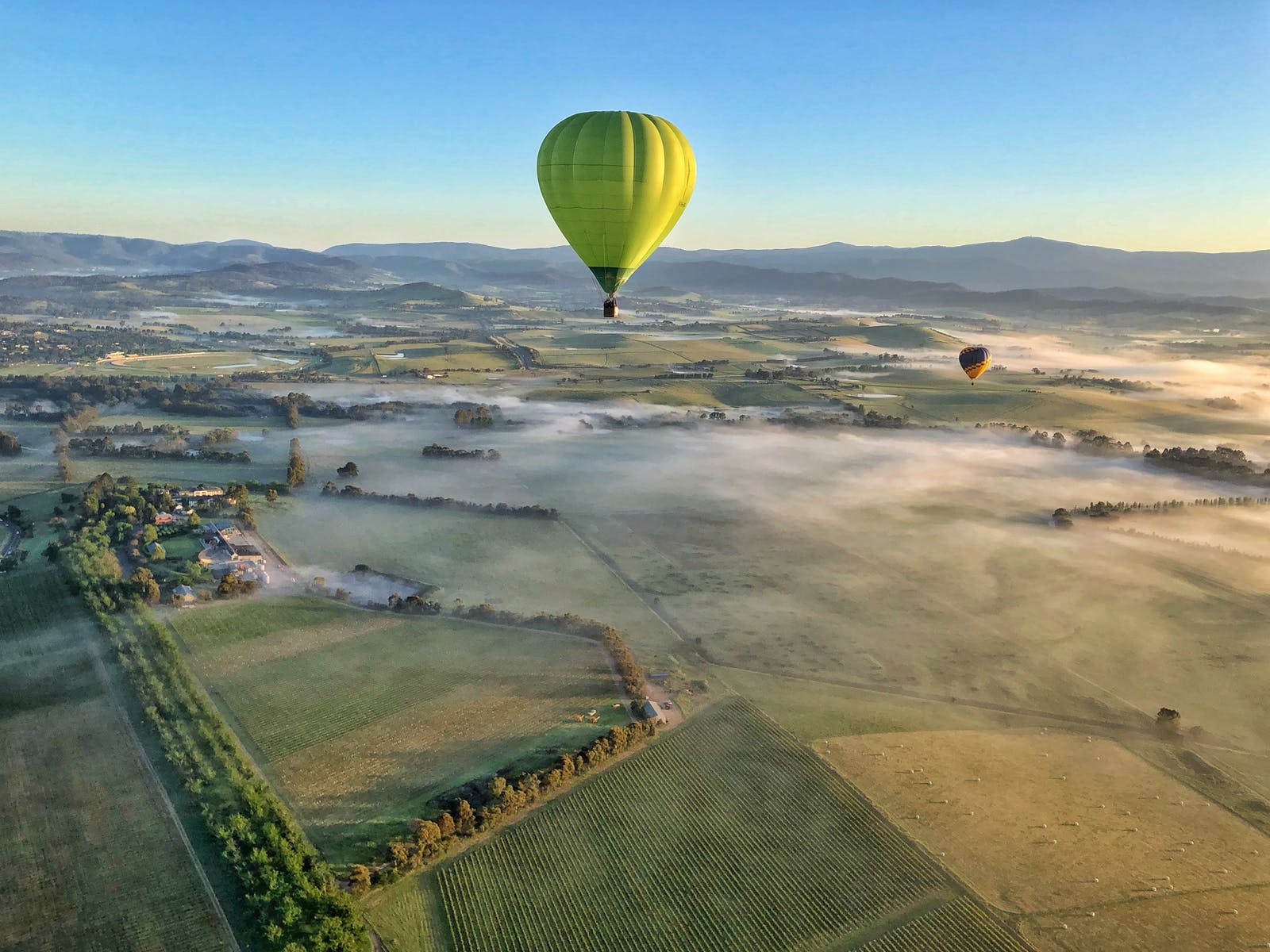 Green hot air balloon sailing over fields